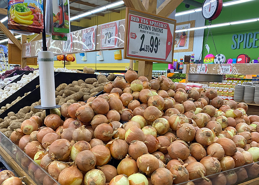 A display of onions with accompanying signage in a produce department.