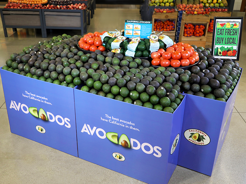A display bin containing avocados, set inside a grocery store