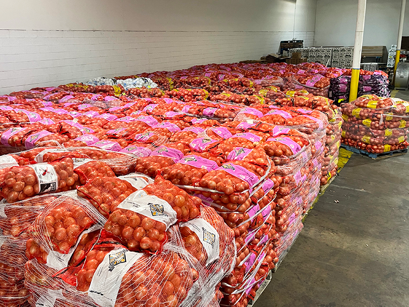 A store room including many pallets loaded with large bags of onions.