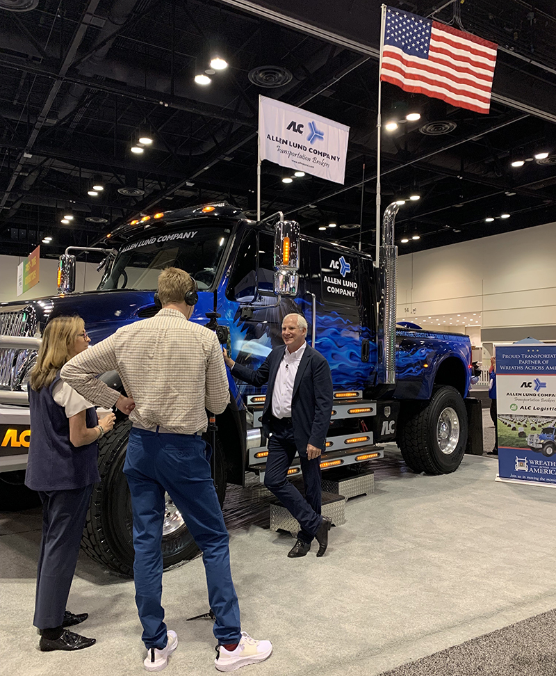 A man stands in front of a truck at a trade show. 