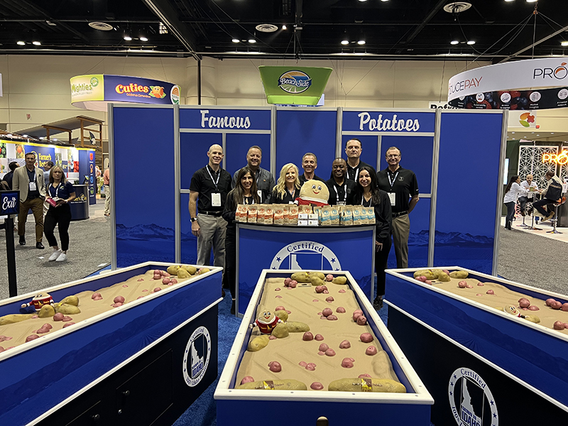 A team of a dozen people dressed in matching blue business attire smile in a Idaho potato booth at the IFPA conference