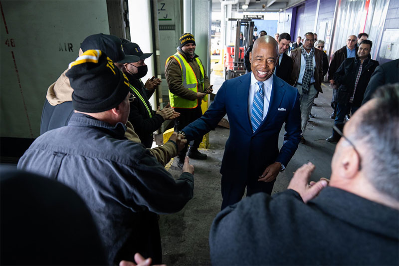 black man in suit shaking hands of blue collar workers white