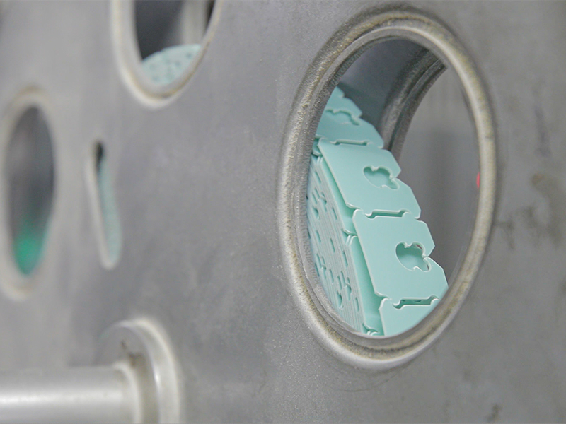 A metal wheel moving strips of bag-closing clips that are seafoam green in color.